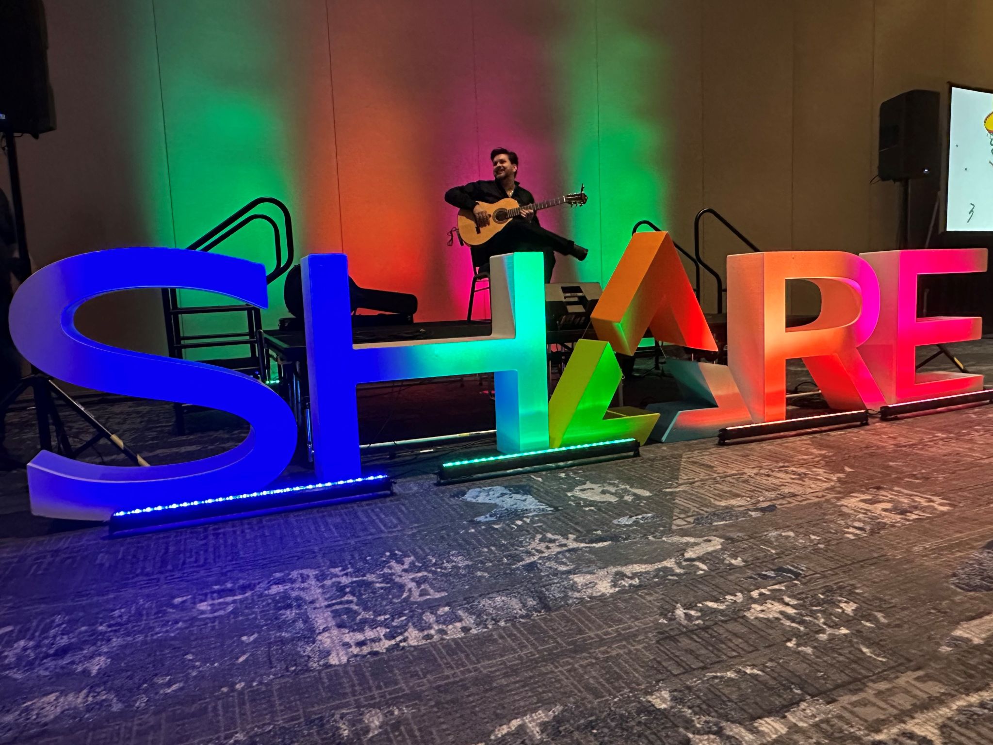 SHARE sign lit up with musician and guitar behind